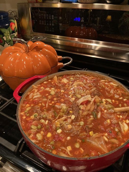 A large stockpot filled with colorful cabbage, corn, and lima beans in tomato broth.
