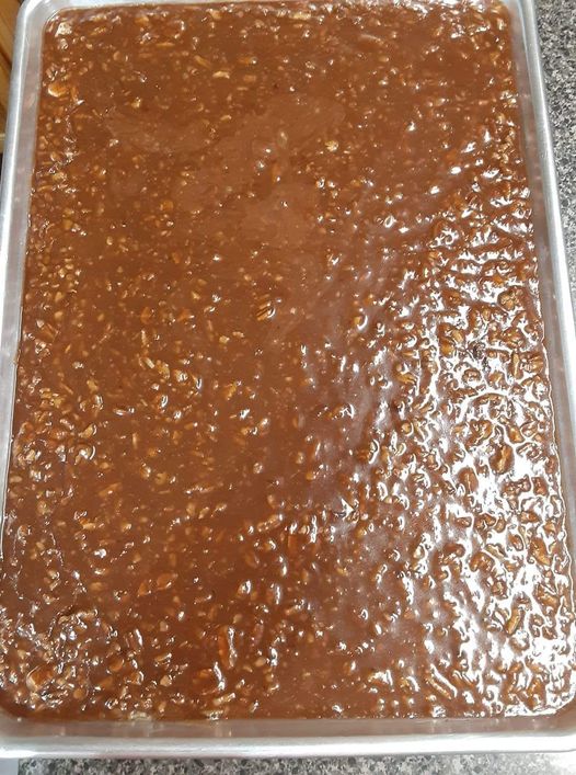 Smooth chocolate fudge mixture with plenty of pecans spread evenly in a silver baking sheet.