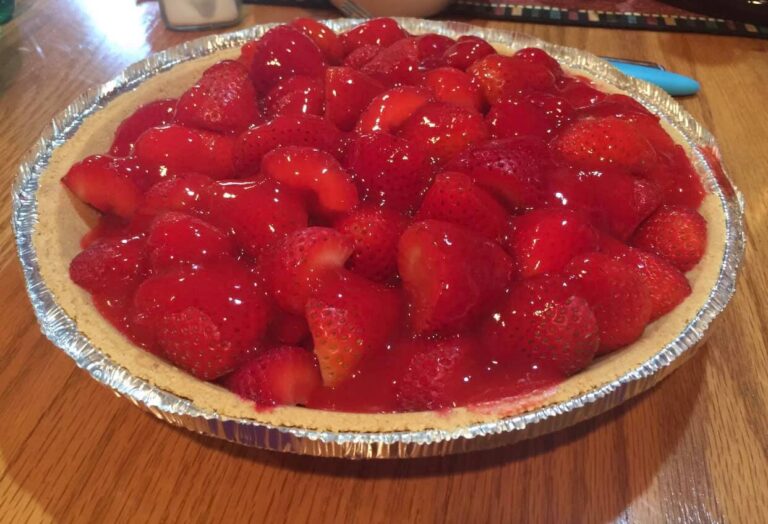 Homemade strawberry pie setting in a silver foil pan on a wooden table.