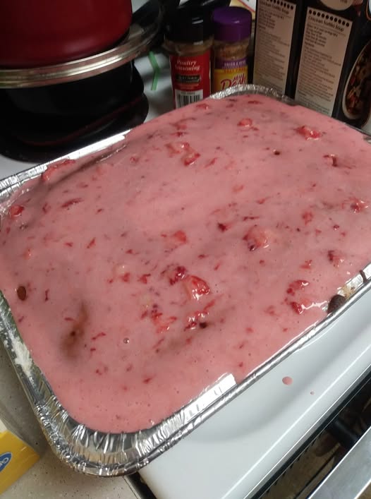 Homemade strawberry sheet cake being prepared with a fresh fruit and cream cheese icing.