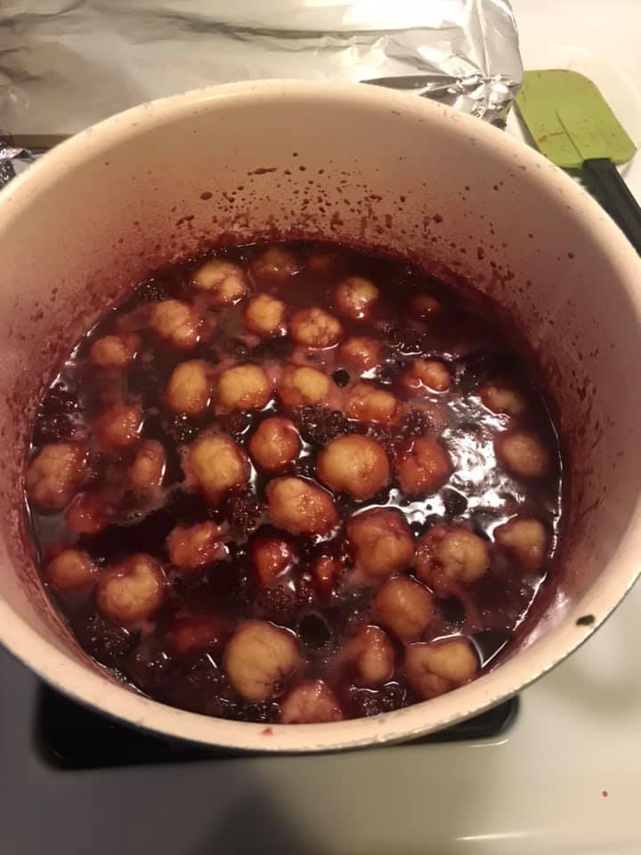 Close up of fluffy pastry balls in a rich, bubbling berry syrup.